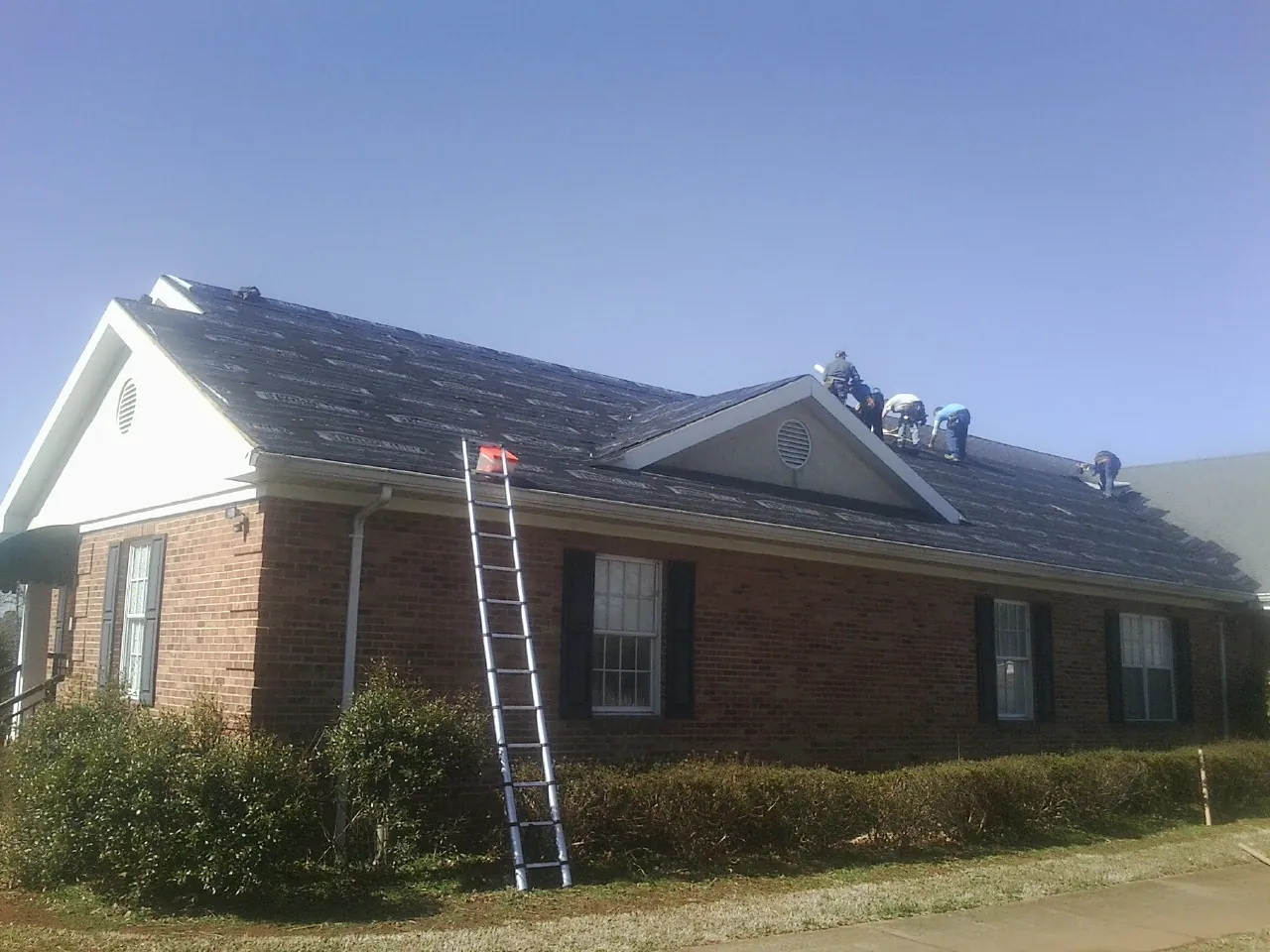 Crew tearing shingles off a brick ranch roof with a ladder set — Metal Roof Repair work by our crew in Morgan