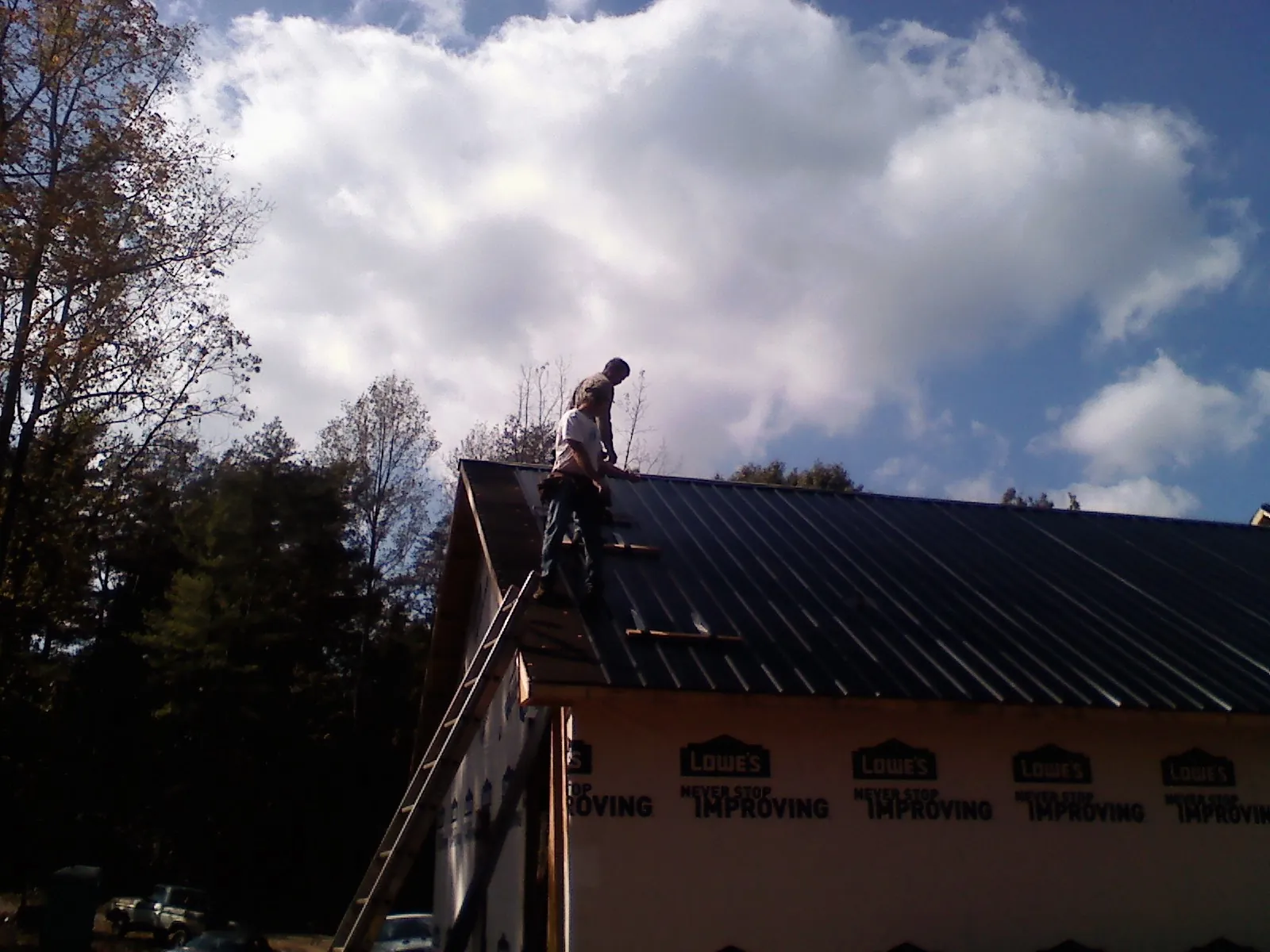 Roofer fastening dark metal panels high against a cloudy sky, from a Roof Inspection job in Morgan